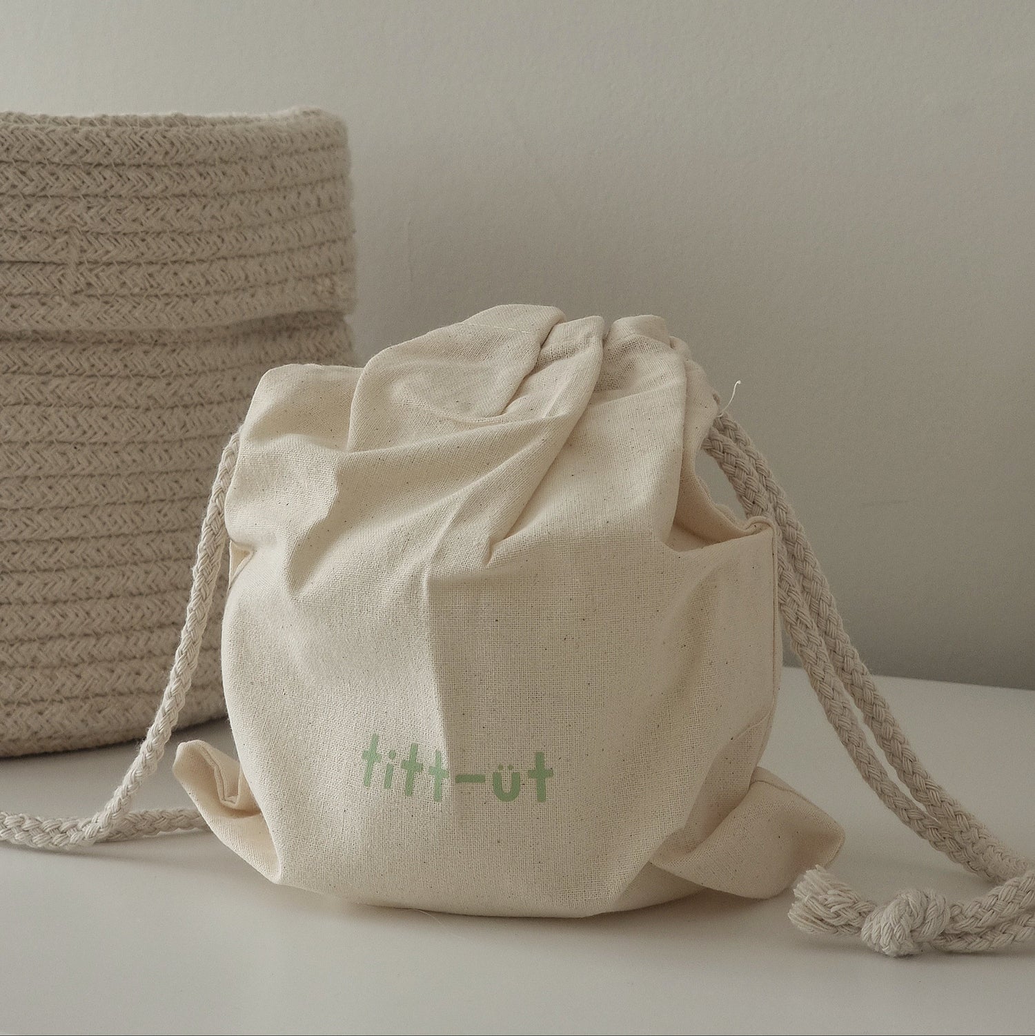 Beige recycled cotton drawstring bag with 'titt-ut' text on a light surface.