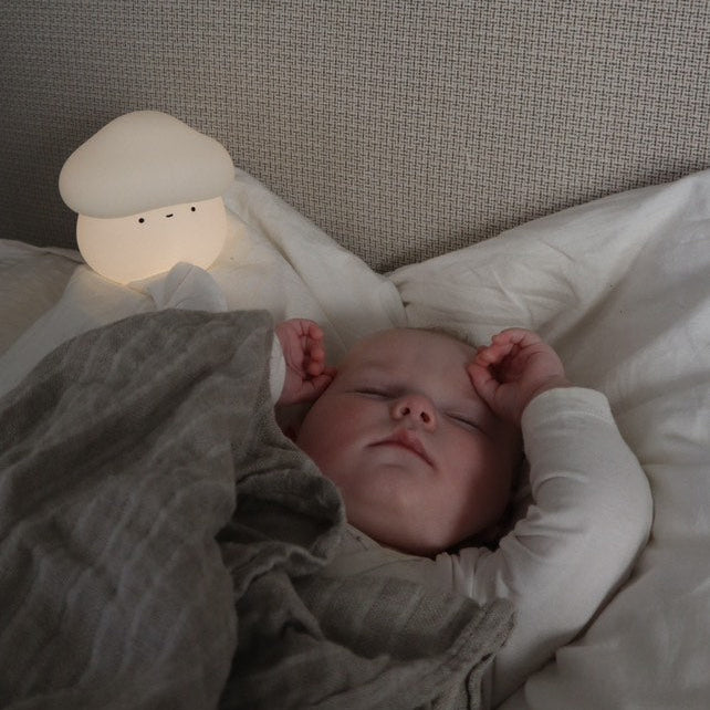 Baby sleeping in bed with a night light and gray blanket